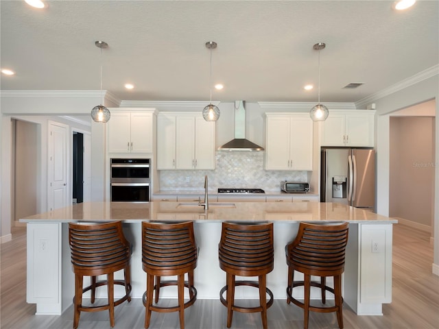kitchen with decorative backsplash, wall chimney exhaust hood, a spacious island, white cabinetry, and appliances with stainless steel finishes