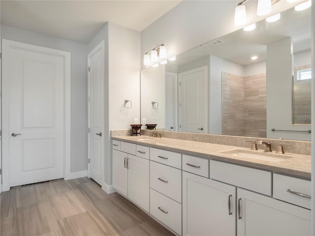 full bath with baseboards, a sink, double vanity, and a tile shower