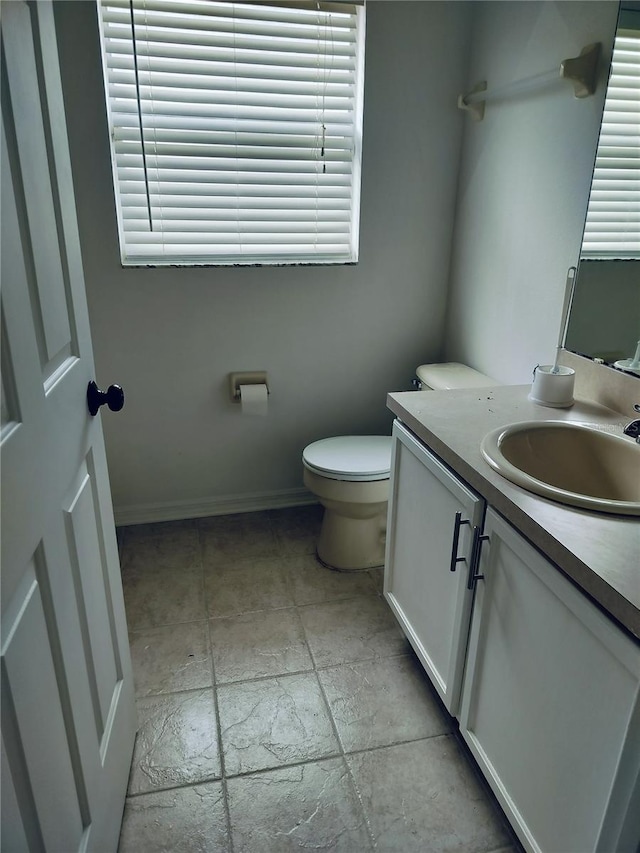 bathroom with baseboards, toilet, vanity, and stone tile floors