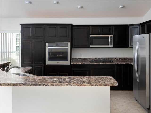 kitchen featuring stainless steel appliances, a sink, dark cabinetry, and light tile patterned floors