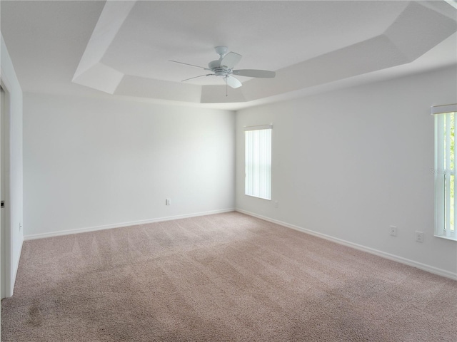 unfurnished room featuring a raised ceiling, ceiling fan, light colored carpet, and baseboards