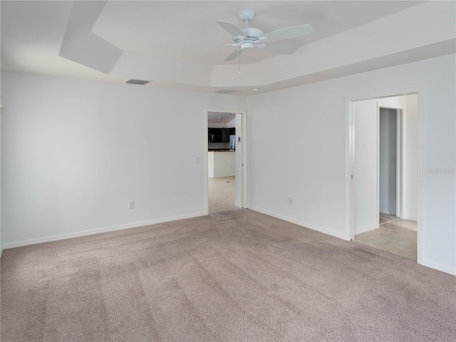spare room featuring carpet floors, a raised ceiling, ceiling fan, and baseboards