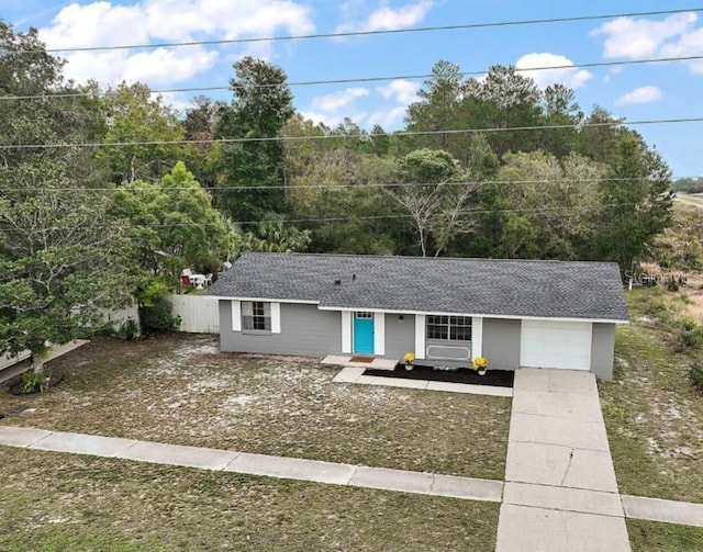 ranch-style home with driveway, a garage, fence, and roof with shingles