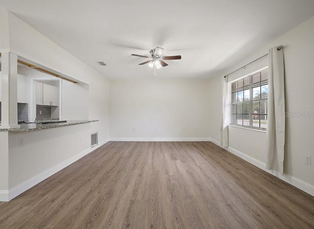 unfurnished living room with a ceiling fan, wood finished floors, baseboards, and visible vents
