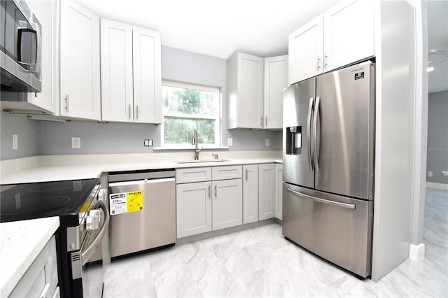 kitchen with white cabinetry, appliances with stainless steel finishes, marble finish floor, a sink, and baseboards