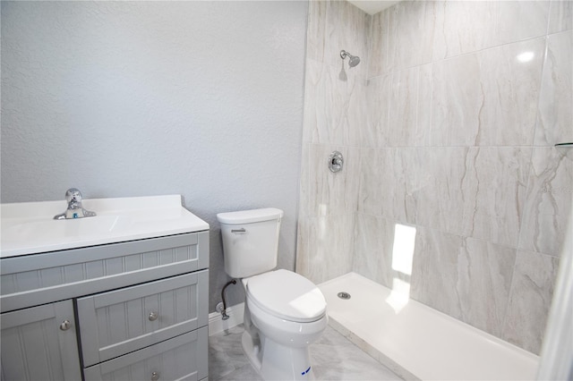 bathroom featuring toilet, tiled shower, vanity, and a textured wall