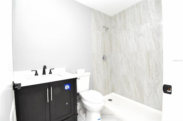 bathroom with toilet, tiled shower, vanity, and a textured wall