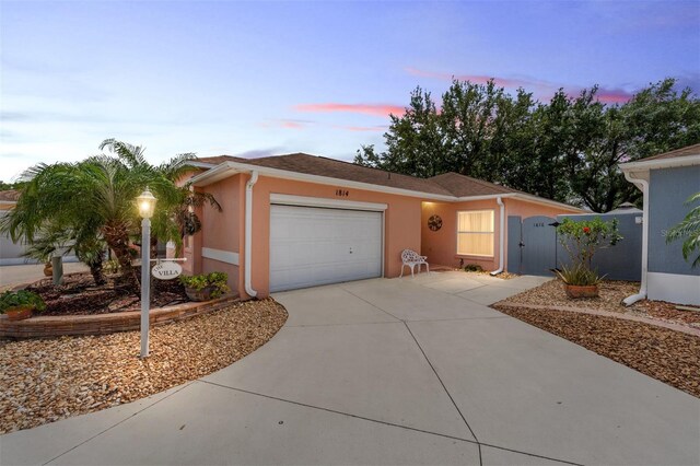 ranch-style house with an attached garage, driveway, stucco siding, and a gate
