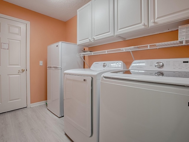910 Eagles Lndg, Leesburg, FL 34748 - laundry room with washing machine and clothes dryer, cabinet space, baseboards, a textured ceiling, and light wood-type flooring