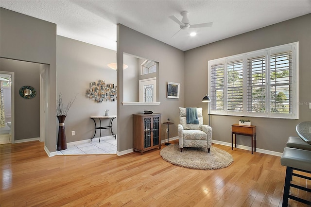 living area featuring a textured ceiling, wood finished floors, baseboards, and a ceiling fan