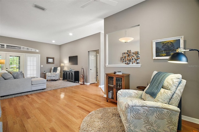 living room featuring visible vents, baseboards, ceiling fan, light wood-type flooring, and lofted ceiling