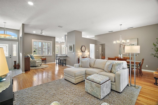 living area with a chandelier, wood finished floors, baseboards, and visible vents