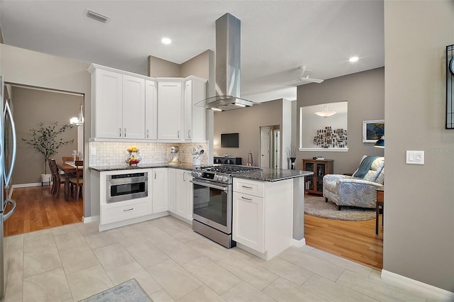 kitchen featuring open floor plan, a peninsula, dark stone counters, stainless steel appliances, and island range hood