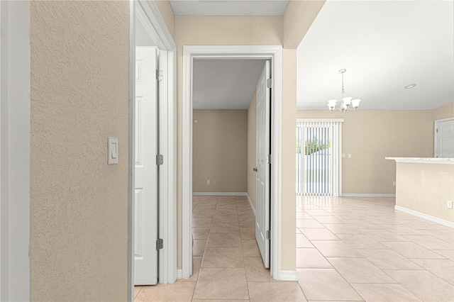 hall featuring baseboards, a textured wall, an inviting chandelier, and light tile patterned flooring