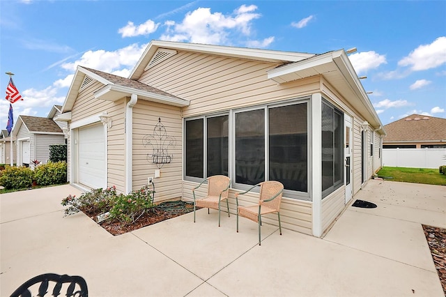 rear view of property with fence, driveway, an attached garage, a patio area, and a sunroom