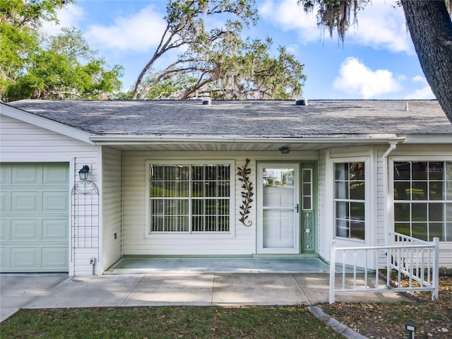 doorway to property with a shingled roof and a garage
