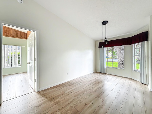 spare room featuring baseboards, vaulted ceiling, wood finished floors, and a textured ceiling