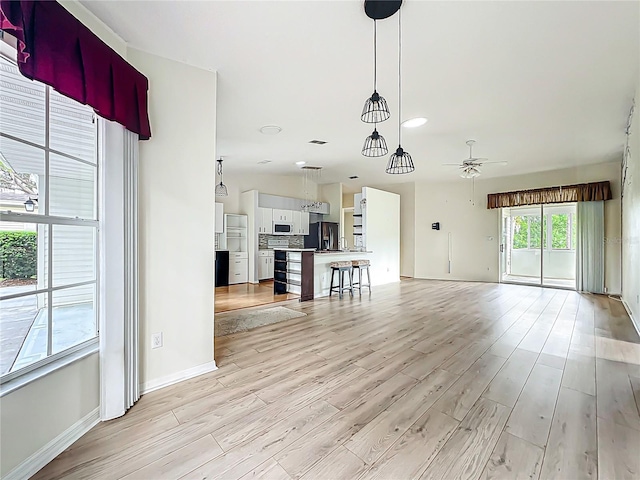 unfurnished living room with baseboards, light wood finished floors, and ceiling fan