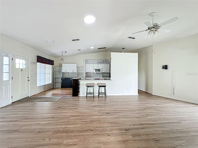 kitchen featuring white microwave, visible vents, vaulted ceiling, and open floor plan