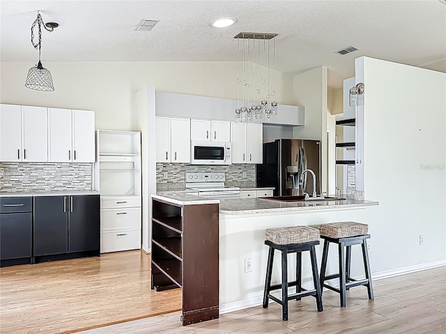 kitchen with a breakfast bar, white cabinetry, visible vents, and white appliances