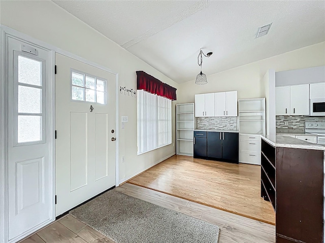kitchen with light countertops, white cabinetry, tasteful backsplash, visible vents, and light wood-style floors