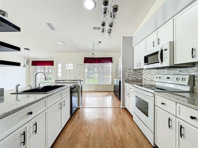 kitchen with a sink, light wood finished floors, white appliances, visible vents, and white cabinets