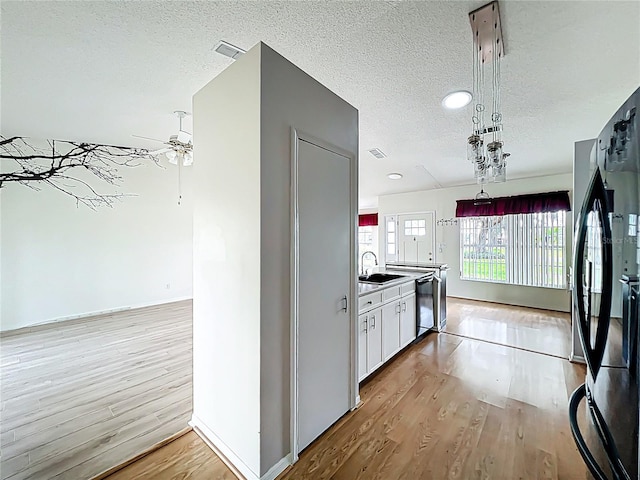 kitchen with white cabinetry, dishwashing machine, a sink, freestanding refrigerator, and light wood-style flooring