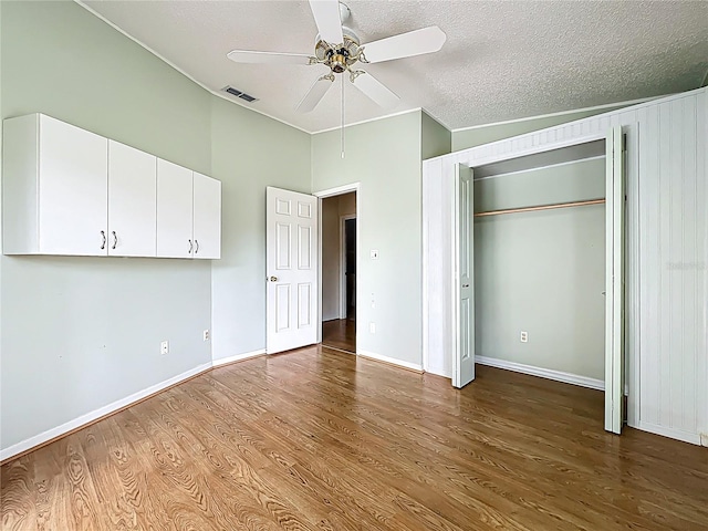 unfurnished bedroom with a textured ceiling, visible vents, baseboards, wood finished floors, and a ceiling fan