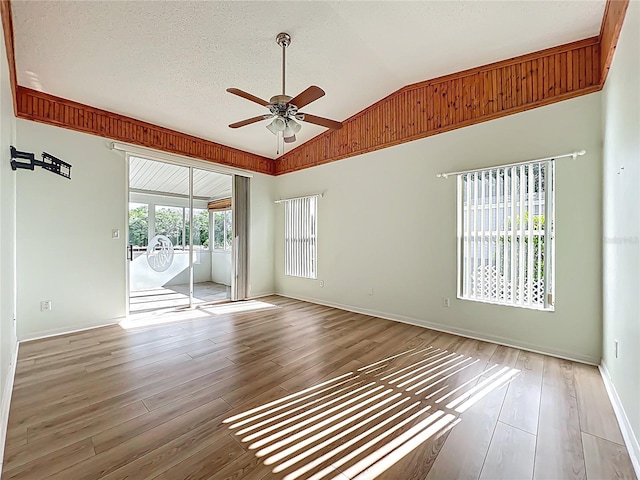 empty room featuring a textured ceiling, lofted ceiling, wood finished floors, and a ceiling fan