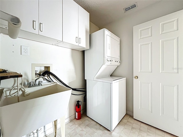 clothes washing area with a sink, stacked washer and dryer, cabinet space, and visible vents