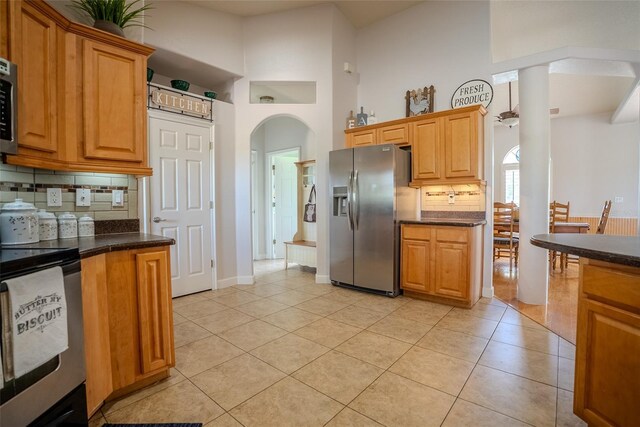 15141 Farm Rd, Groveland, FL 34736 - kitchen featuring light tile patterned flooring, backsplash, stainless steel appliances, arched walkways, and a towering ceiling