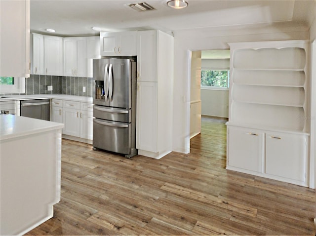 kitchen with light countertops, white cabinetry, stainless steel appliances, backsplash, and light wood-style flooring
