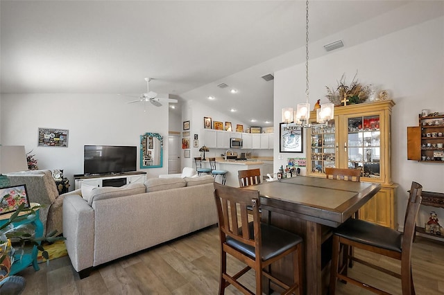 dining area featuring ceiling fan with notable chandelier, light wood-style flooring, visible vents, and vaulted ceiling