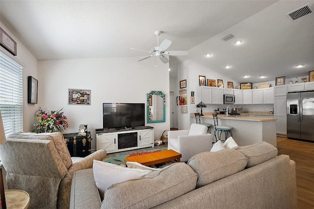 living area with wood finished floors, visible vents, vaulted ceiling, and a ceiling fan