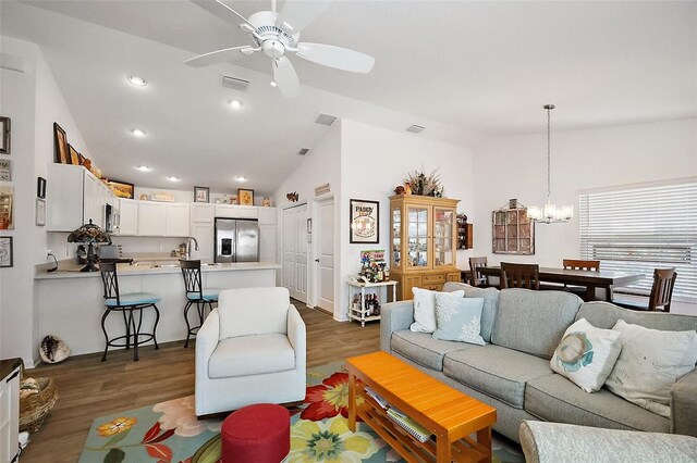 living room with wood finished floors, ceiling fan with notable chandelier, lofted ceiling, visible vents, and recessed lighting