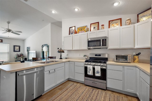 kitchen with a peninsula, a toaster, a sink, vaulted ceiling, and appliances with stainless steel finishes