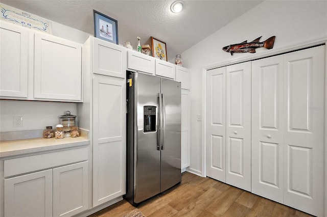 kitchen featuring white cabinets, stainless steel fridge with ice dispenser, light countertops, light wood-type flooring, and a textured ceiling
