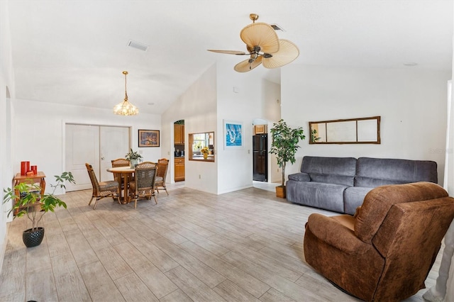 living area with high vaulted ceiling, ceiling fan, light wood-style flooring, a chandelier, and baseboards