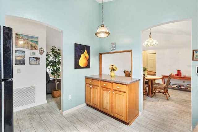 kitchen with arched walkways, freestanding refrigerator, light wood-style floors, a chandelier, and decorative light fixtures