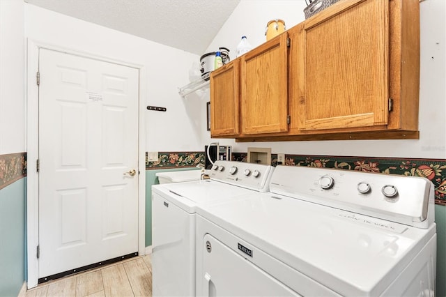 clothes washing area featuring cabinet space, washing machine and clothes dryer, light wood-style floors, and a textured ceiling
