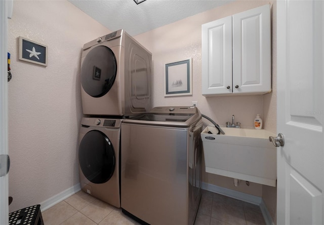 washroom featuring baseboards, light tile patterned flooring, stacked washing maching and dryer, cabinet space, and a sink