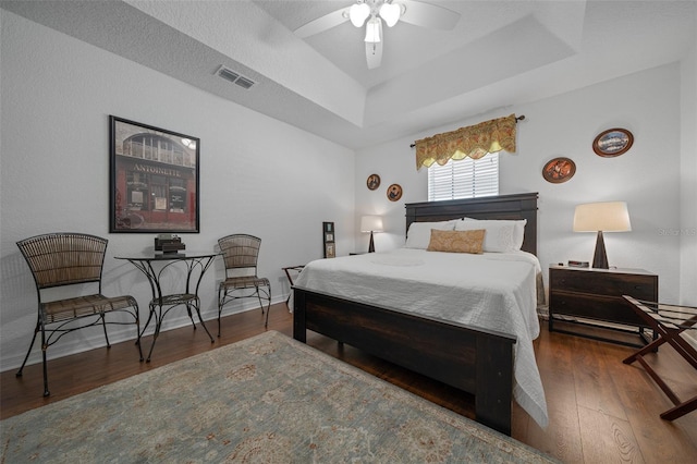 bedroom with baseboards, a ceiling fan, visible vents, a tray ceiling, and wood finished floors
