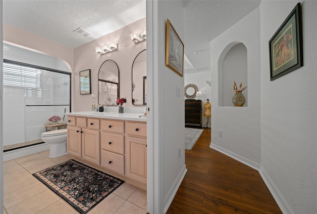 full bathroom with visible vents, toilet, a textured ceiling, double vanity, and a shower with door