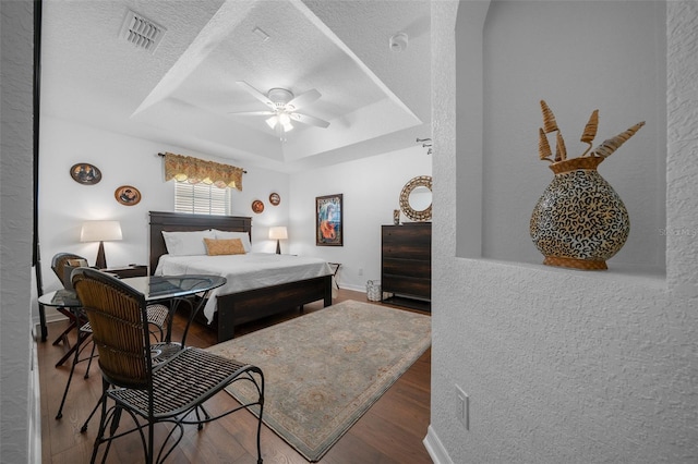bedroom with visible vents, a raised ceiling, a ceiling fan, a textured ceiling, and wood finished floors