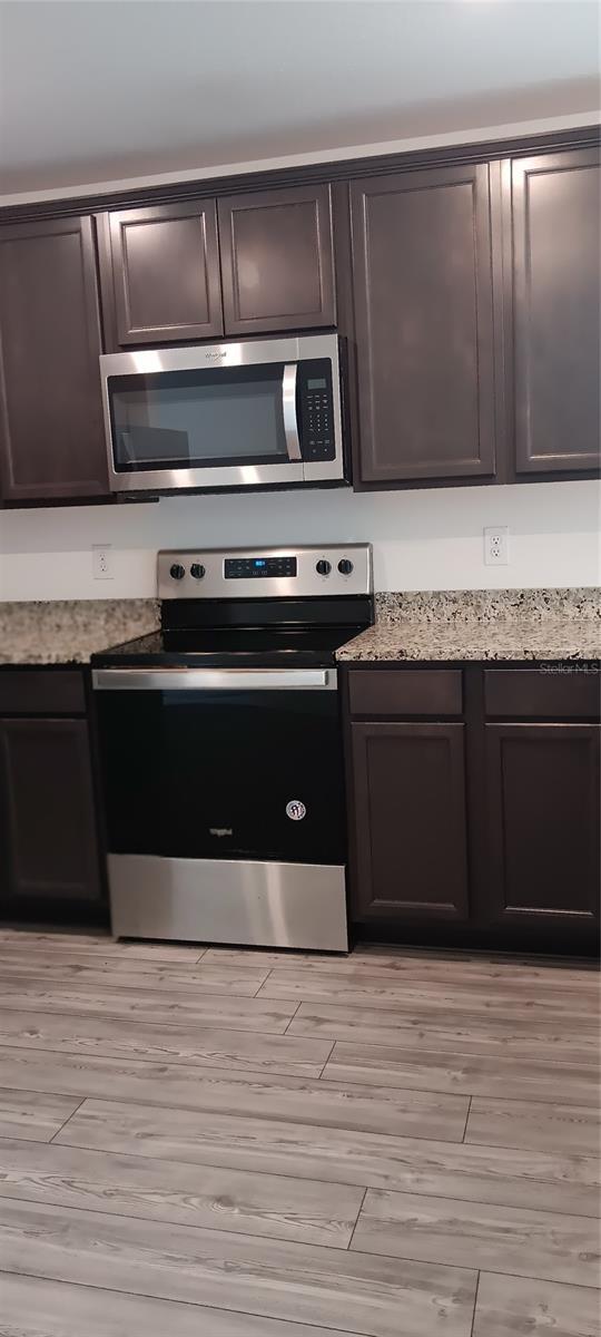 27 Perch Dr, Kissimmee, FL 34759 - kitchen featuring stainless steel appliances, dark brown cabinets, light wood-type flooring, and light stone counters