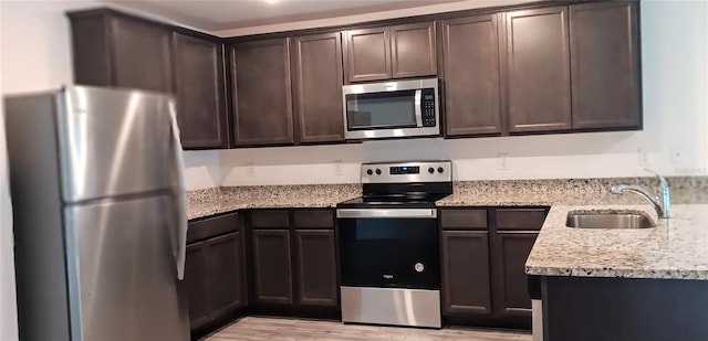 27 Perch Dr, Kissimmee, FL 34759 - kitchen featuring stainless steel appliances, a sink, dark brown cabinets, light stone counters, and light wood-type flooring