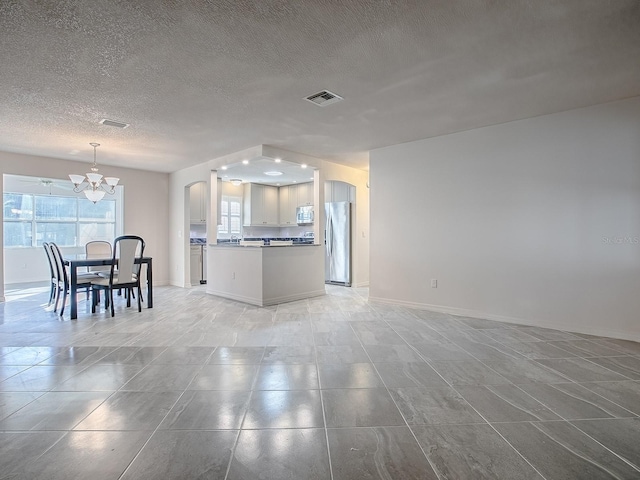 living area featuring a chandelier, a textured ceiling, arched walkways, and visible vents