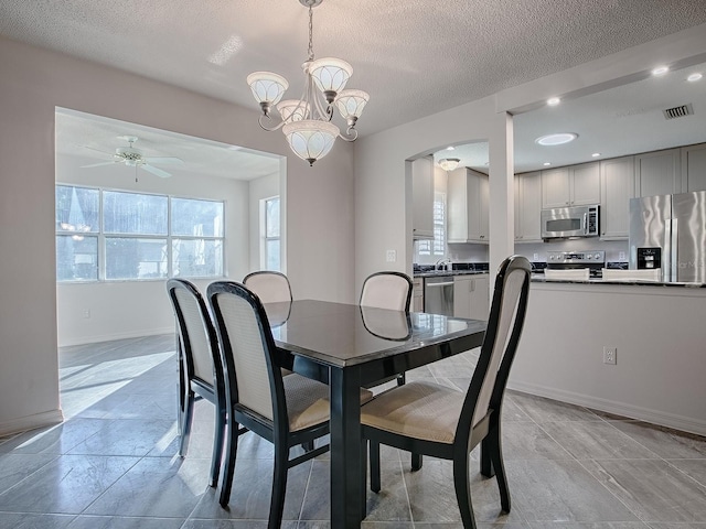 dining room featuring a textured ceiling, ceiling fan with notable chandelier, arched walkways, baseboards, and visible vents