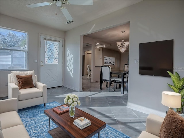 living room with baseboards, tile patterned floors, visible vents, and ceiling fan with notable chandelier