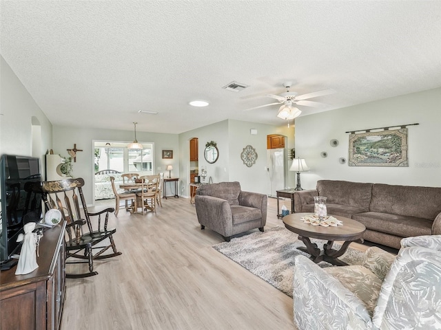 living area featuring visible vents, arched walkways, ceiling fan, light wood-style floors, and a textured ceiling